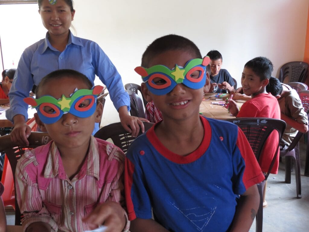 Two children wearing paper masks and sitting in a classroom.